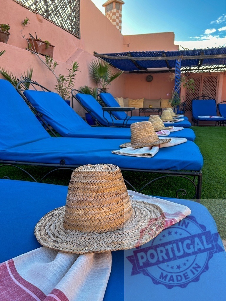 Straw hats resting on blue sunbeds in a Moroccan riad | Sunbathing area in a Moroccan riad with straw hats and towels on blue sunbeds - Realized with Pictrs.com