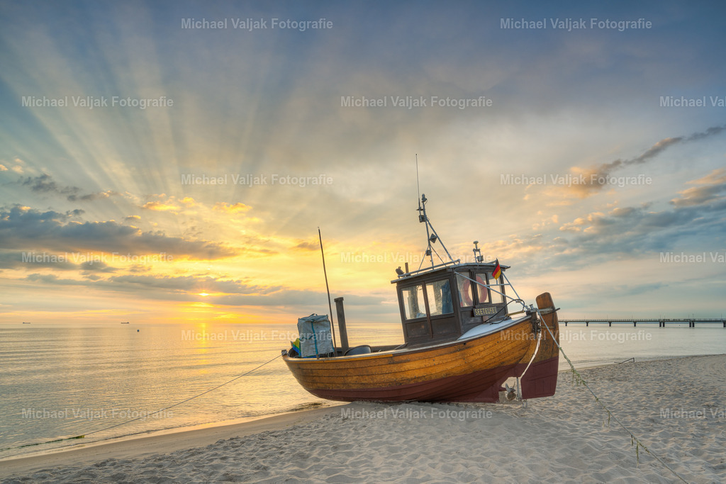 Fischerboot am Strand auf Usedom | Einsam und verlassen liegt das kleine Fischerboot "Seeteufel" am Sandstrand auf Usedom. Im Hintergrund ein herrlicher Sonnenaufgang, die Sonne schaut kurz durch eine Wolkenlücke und fächerartig breiten sich die Sonnenstrahlen aus. Eine einmalige Stimmung an einem schönen Sommermorgen.  - Realisiert mit Pictrs.com