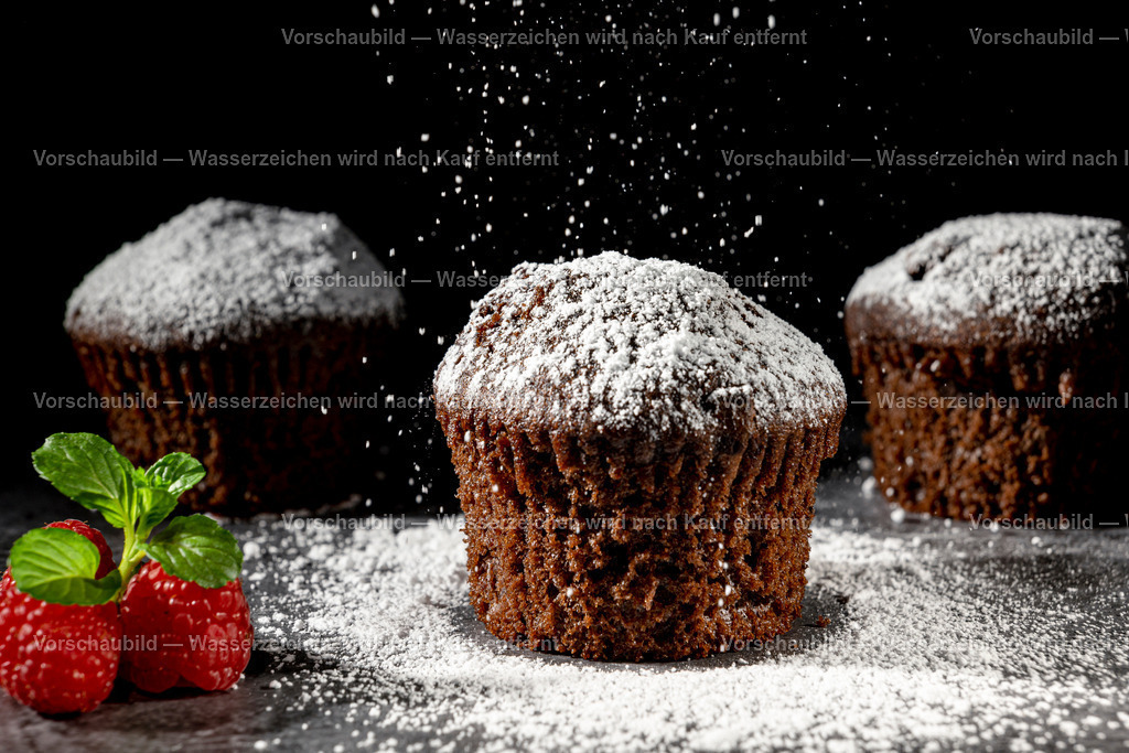 Schokomuffins werden mit Puderzucker bestreut | Schokomuffins werden mit Puderzucker bestreut., Dekoriert mit Himbeeren und Minzblatt. Low Key Aufnahme - Realisiert mit Pictrs.com