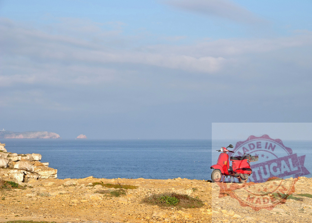 Red scooter parked on coastal cliff overlooking ocean. Centro - Portugal | Red scooter resting on a cliff edge with ocean and sky, symbolizing travel and freedom - Realized with Pictrs.com