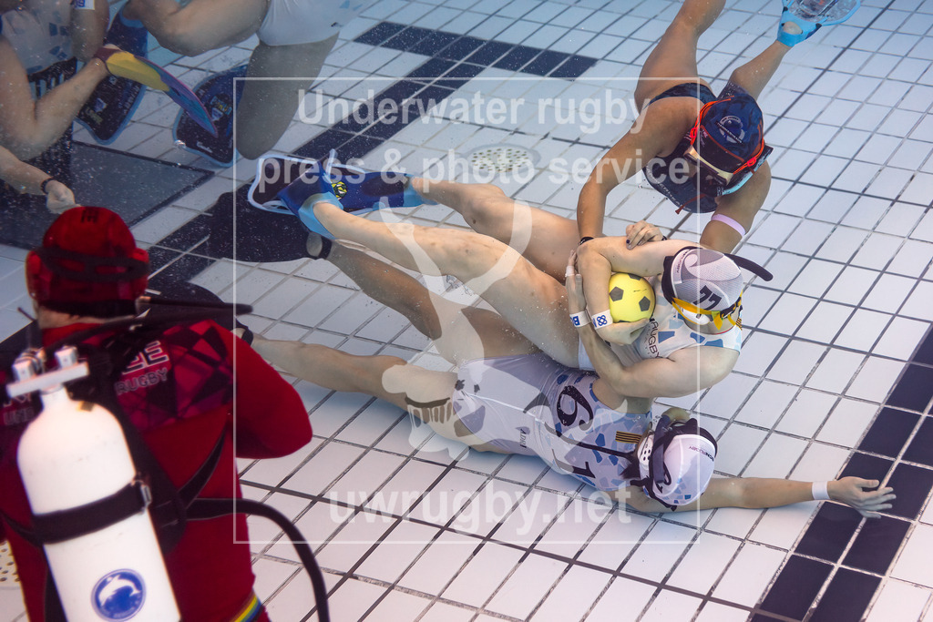 24. - 26.11.2023: Unterwasser-Rugby Champions Cup 2023  | Damen-Spiel: NJ Hammerheads (USA) in blau gegen Barcelona (Spanien) in weiß.  Ines de Gregorio (weiß #77) bringt den Spielball in einen sichenern Abstand vom eigenen Tor und wird dabei von einer Amerikanierin angegriffen. - Realisiert mit Pictrs.com