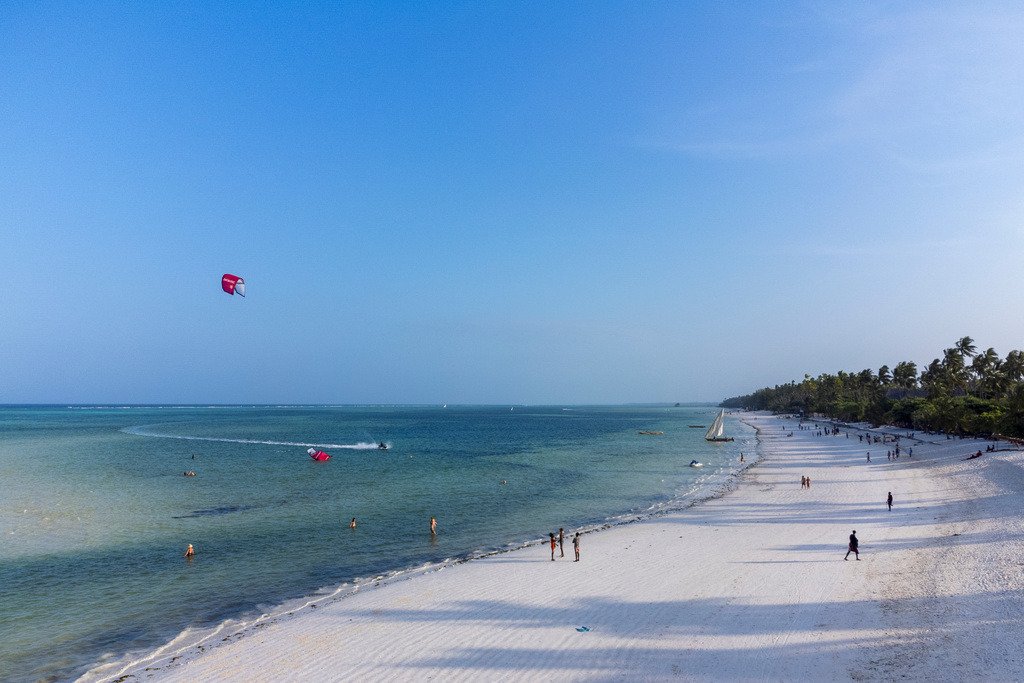 Zanzibar Beach Serenity | Zanzibar’s expansive coastline, with kite surfers in the distance and peaceful beachgoers enjoying the serene beauty of the shore.
