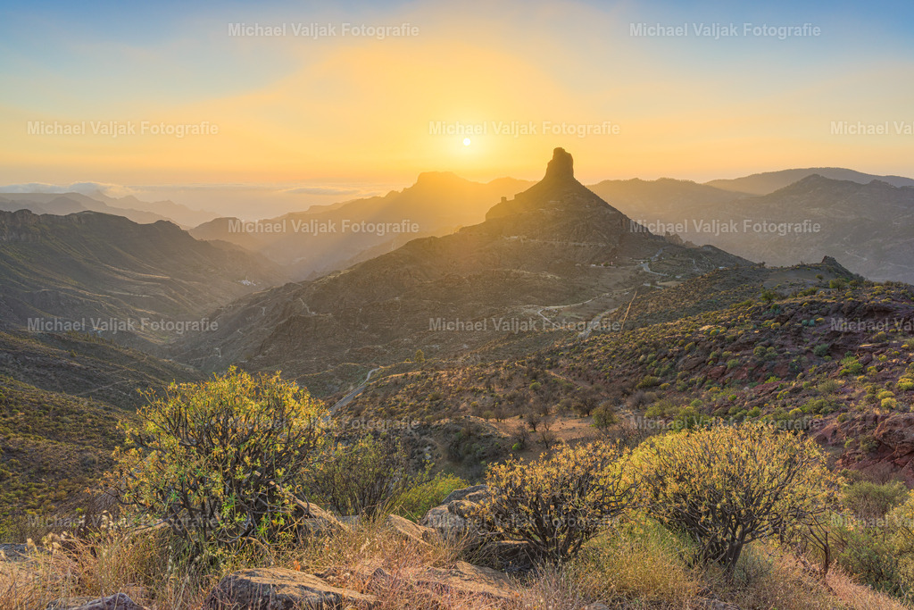 Roque Bentayga auf Gran Canaria | Der Roque Bentayga, mitten im Bergland von Gran Canaria, zeigt sich im Licht des Sonnenuntergangs von seiner eindrucksvollsten Seite. Die warmen Farben des Himmels – zwischen Orange und Violett – verleihen der kargen Landschaft eine weiche, fast friedliche Stimmung.Der markante Fels, einst heiliger Ort der Ureinwohner, steht ruhig und unverändert inmitten der weiten Szenerie. Um ihn herum beginnen die Täler in der Dämmerung zu verschwinden – ein Moment, der gleichzeitig schlicht und besonders wirkt.Ein Bild, das die stille Seite Gran Canarias zeigt – fernab vom Trubel der Küste. - Realisiert mit Pictrs.com