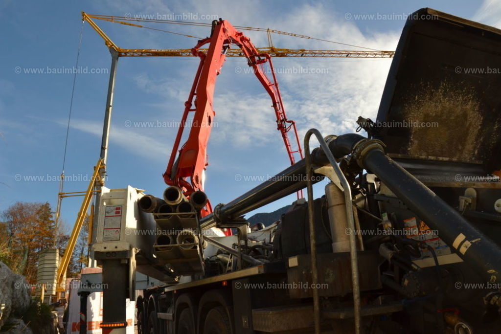 Autobetonpumpe und Baukran | Autobetonpumpe mit ausgefahrenem Betonverteilermast, dahinter Baukran, Hintergrund blauer Himmel mit Wolken