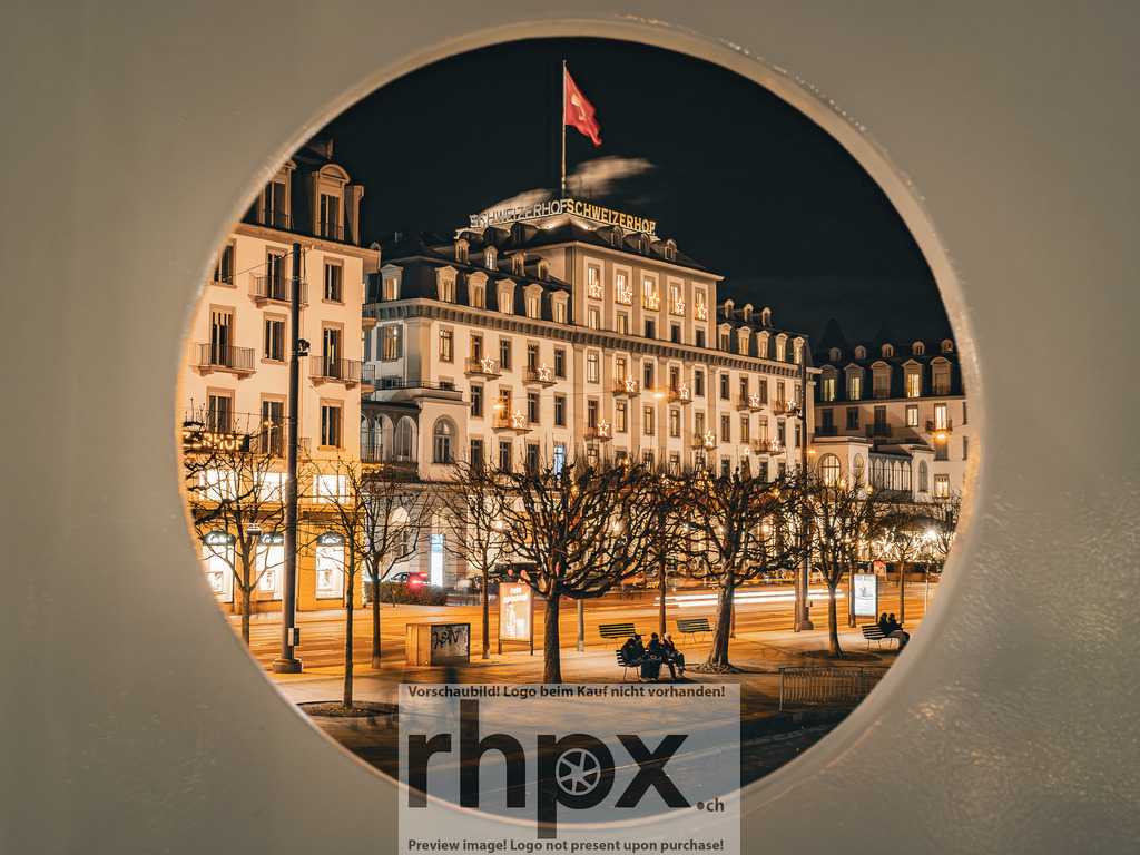 Blick auf den Schweizerhof | Tradition. Licht. Fokus.Die historische Fassade des Hotel Schweizerhof wird durch die kreisrunde Öffnung eines Schiffes perfekt eingerahmt. Diese ungewöhnliche Perspektive verleiht dem Luzerner Wahrzeichen in der nächtlichen Dunkelheit eine ganz besondere Tiefe.Wähle unter "Produktauswahl" dein Wunschformat: Vom klassischen Wandbild über Puzzle &amp; Tassen bis zum digitalen Download (z.B. als Handy-Hintergrund). - Realisiert mit Pictrs.com