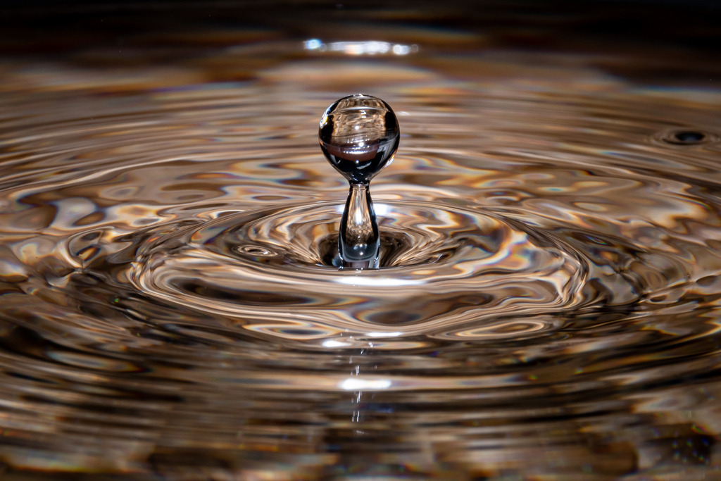 Wassertropfen | Das Bild zeigt einen Wassertropfen, der von oben in eine klare, ruhige Wasseroberfläche fällt. Der Moment, in dem der Tropfen die Oberfläche durchbricht, erzeugt eine feine, kreisförmige Welle, die sich sanft ausbreitet. Der Tropfen selbst erscheint als kleiner, runder Fleck in der Mitte des Kreises, während er schnell in das Wasser eintaucht.

Sobald der Tropfen das Wasser erreicht, entsteht ein kurzes, aber kraftvolles Geräusch, begleitet von einem Spritzer aus Wasser, der in alle Richtungen spritzt. Dann beginnt der Tropfen aufgrund des Auftriebs schnell wieder nach oben zu steigen und bildet einen dünnen Strahl aus Wasser, der sich schnell verjüngt, bis er schließlich verschwindet.

In diesem kurzen Moment wird die Schönheit und Anmut der Natur in all ihrer Einfachheit gezeigt, während der Tropfen in eine Welt von Wasser und Wellen eintaucht und wieder auftaucht.