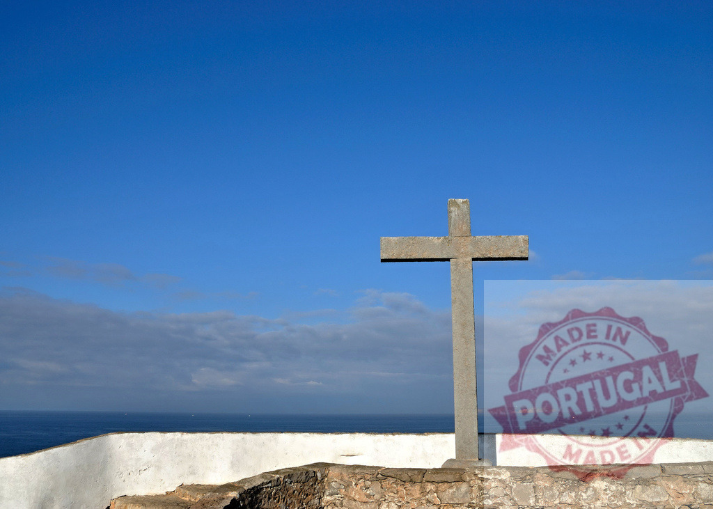Stone Christian cross standing by ocean under blue sky. Centro - Portugal | Stone cross standing on a wall overlooking the ocean under a clear blue sky - Realized with Pictrs.com