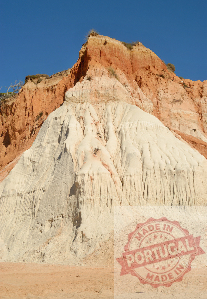 Layered rock cliff formation displaying erosion under clear sky | Layered rock formations show colors of white and orange under a blue sky - Realisiert mit Pictrs.com