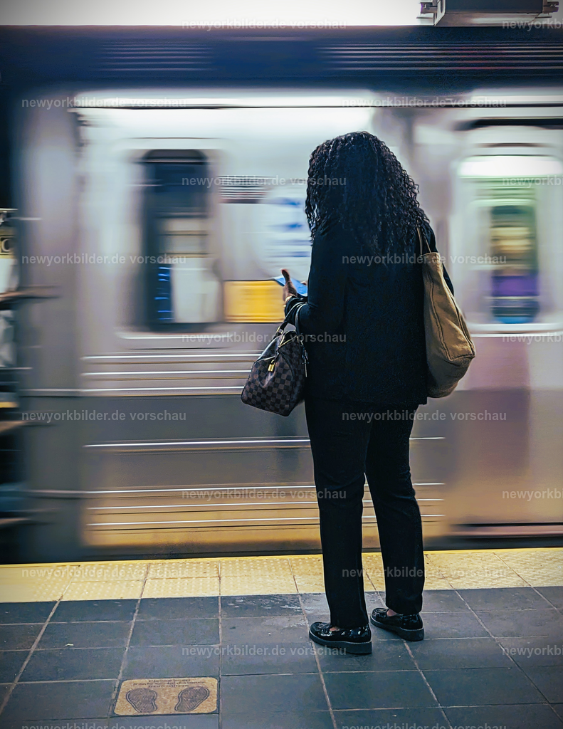 Dynamik im Untergrund – Frau wartet in der New Yorker Subway, Zug rauscht vorbei | Die Subway ist das pulsierende Herz von New York City – ein Ort voller Geschichten, Begegnungen und Bewegung. Dieses Bild fängt einen Moment ein, der die Dynamik des Untergrunds perfekt widerspiegelt: Eine Frau steht geduldig am Bahnsteig, während ein Zug mit hoher Geschwindigkeit vorbeirauscht. Die Lichter des Zuges ziehen wie Streifen durch die Dunkelheit, ein visuelles Symbol für die Geschwindigkeit und den Rhythmus der Metropole. Hier unten ist die Stadt anders – roh, authentisch, voller Energie. Gespräche, Musik, das metallische Rattern der Gleise: all das verschmilzt zu einem urbanen Soundtrack, der niemals endet. Trotz aller Herausforderungen bleibt die Subway der schnellste Weg, um die Stadt zu erleben, und sie erzählt Geschichten von Millionen Menschen, die täglich unterwegs sind. 