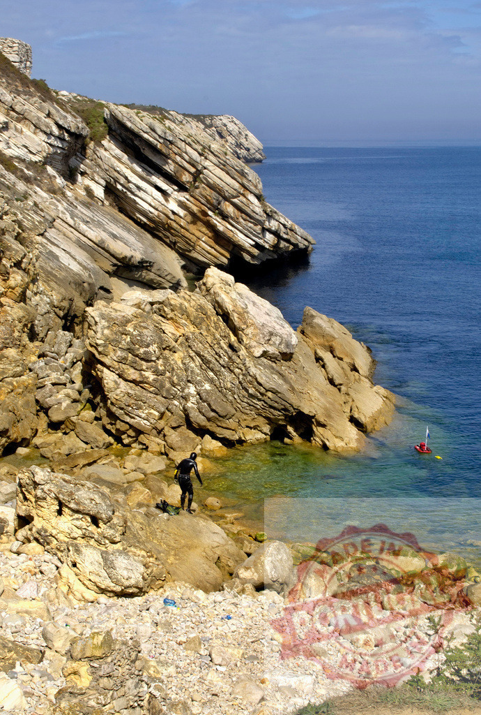 Diver spearfishing exploring rocky coastline clear water | Diver in wetsuit preparing for spearfishing by rocks near turquoise sea - Realized with Pictrs.com