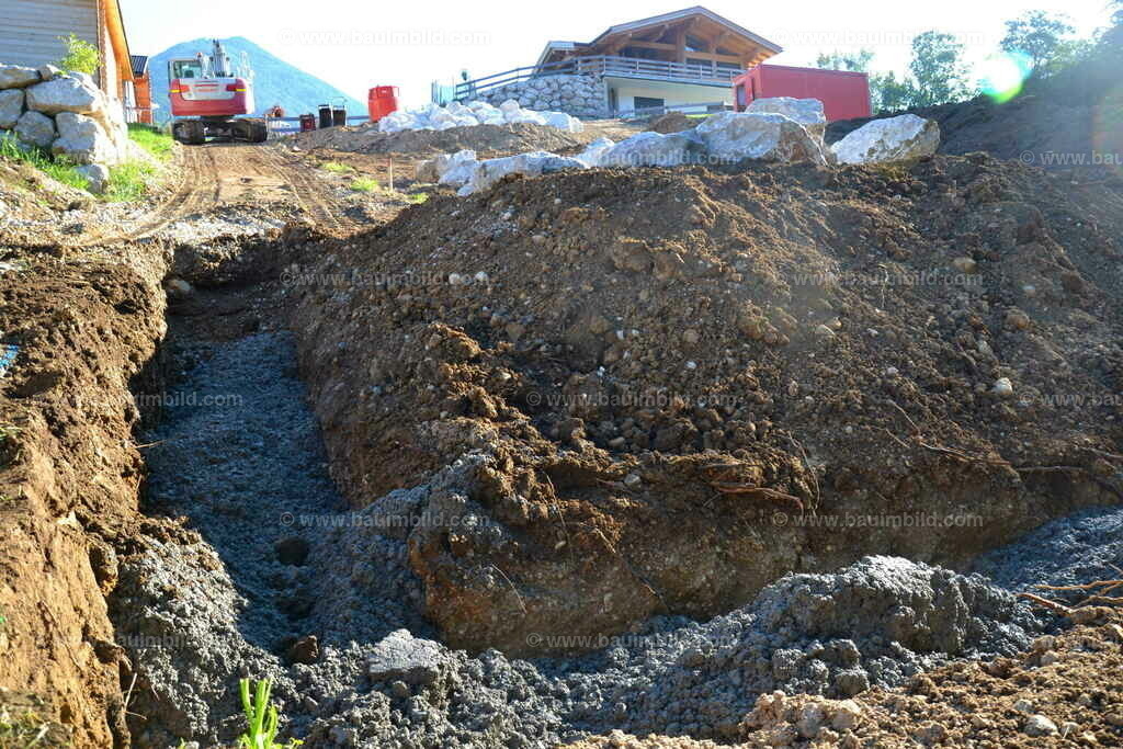 Fundamentgraben mit Magerbeton | Magerbeton in Fundamentgraben für Steinmauer, dahinter Kalksteine und Bagger für Betontransport