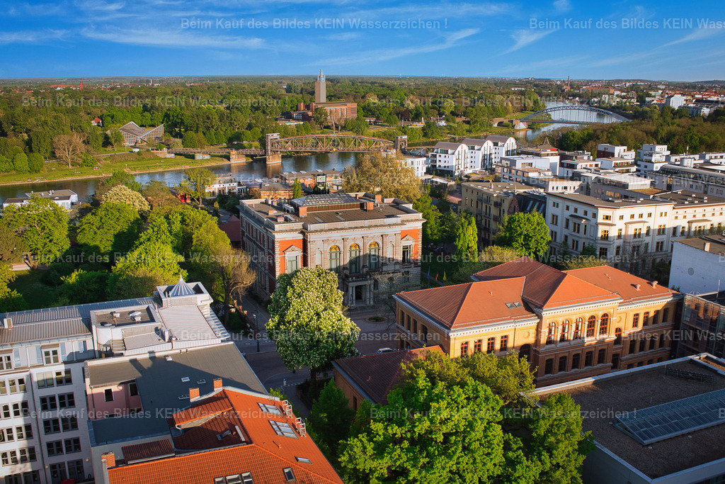 Magdeburg_Luftbild_Staatskanzlei_Palais_Fürstenwall_Hegelstraße_Domgymnasium_Elbe_6758 | Dieses Luftbild zeigt die Staatskanzlei des Landes Sachsen-Anhalt in der Hegelstraße im Herzen von Magdeburg. Bei sonnigem Wetter und klarem blauem Himmel präsentiert sich das repräsentative Gebäude aus einer außergewöhnlichen Perspektive und fügt sich harmonisch in das historische Stadtbild der Landeshauptstadt ein.Die Staatskanzlei ist der Amtssitz des Ministerpräsidenten und das politische Zentrum Sachsen-Anhalts. Von hier aus werden wichtige Entscheidungen für das Bundesland vorbereitet und koordiniert. Aus der Vogelperspektive wird die zentrale Lage des Gebäudes besonders deutlich. Gleichzeitig eröffnet sich ein Blick auf die umgebende Bebauung, die großzügigen Grünflächen sowie die Nähe zur Elbe und zum Domviertel.Das Zusammenspiel aus historischer Architektur, gepflegten Außenanlagen und dem strahlenden Sommerwetter verleiht der Aufnahme eine freundliche und repräsentative Wirkung. Dieses Luftbild dokumentiert nicht nur einen bedeutenden Ort der Landespolitik, sondern zeigt auch die architektonische Vielfalt und Attraktivität Magdeburgs als moderne Landeshauptstadt Sachsen-Anhalts. - Realisiert mit Pictrs.com