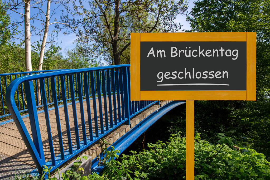Am Brückentag geschlossen | (Fotomontage) Schild mit der Aufschrift AM BRÜCKENTAG GESCHLOSSEN vor einer Brücke im Wald - Realisiert mit Pictrs.com