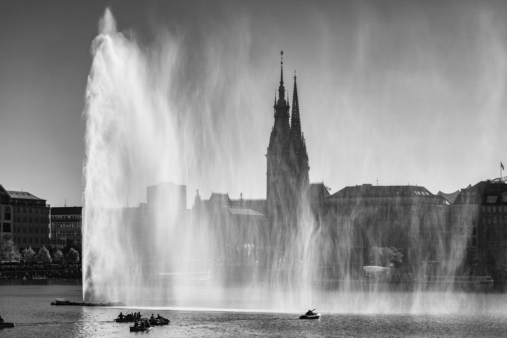 10240304 - Alsterfontäne | Blick auf die Alsterfontäne und das Rathaus im Sonnenlicht, eine eindrucksvolle Schwarzweißaufnahme.