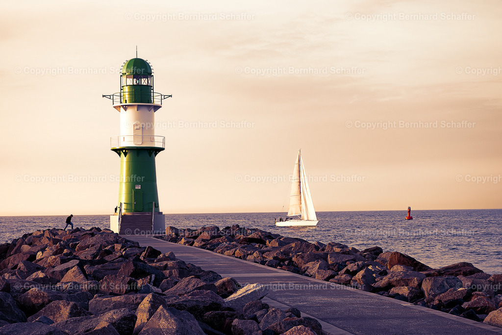 Leuchtturm im Abendlicht | Grüner Leuchtturm an der Ostseeküste neben der Hafeneinfahrt von Warnemünde in Deutschland. Mit einem Segelschiff und einer Boje auf dem Meer im nostalgischen Abendlicht. - Realisiert mit Pictrs.com