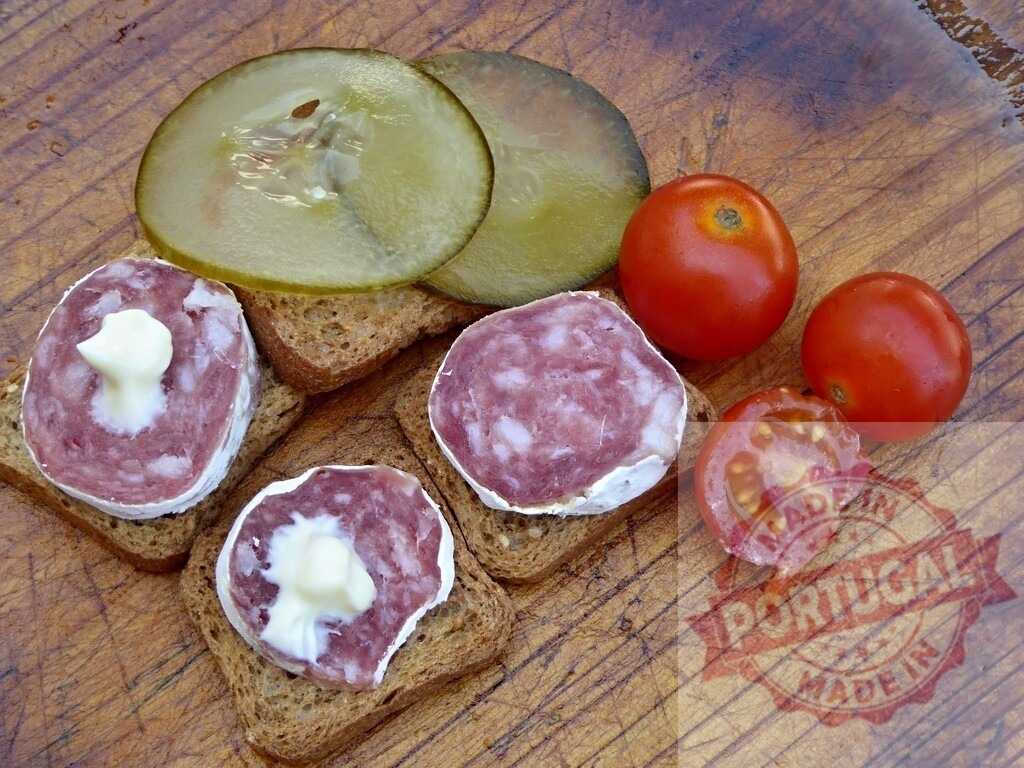 Salami canapés on rye bread with pickles and tomatoes | Salami canapés on rye bread with cream, pickle slices, and fresh tomatoes on a wooden board - Realisiert mit Pictrs.com