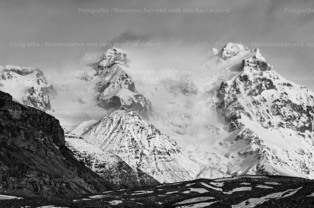 Schneebedeckte Berge in Island | Monochrome Landschaftsaufnahme einer mächtigen Bergkulisse in Island. Die schneebedeckten Gipfel, tiefen Kontraste und dramatischen Wolken verleihen der Szene eine raue, zeitlose und eindrucksvolle nordische Stimmung. - Realisiert mit Pictrs.com