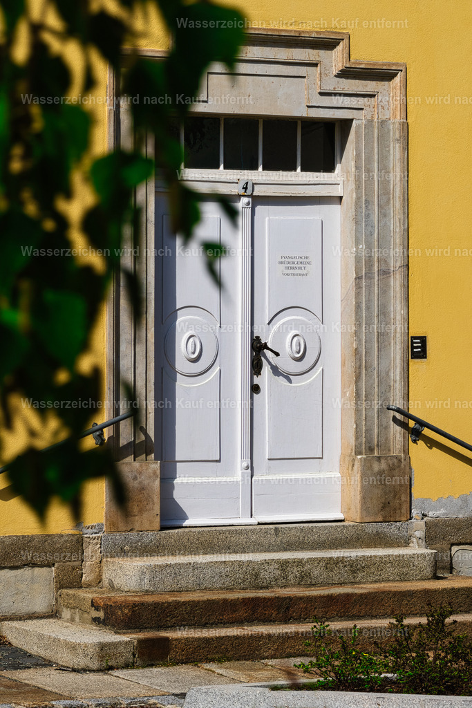 Herrnhut - Zinzendorfplatz, Portal | Zinzendorfplatz in Herrnhut – historischer Mittelpunkt der Stadt mit klassischer Bebauung, viel Grün und besonderem Charme der Herrnhuter Ortsgeschichte. Herrnhut ist eine Stadt im sächsischen Landkreis Görlitz in der Oberlausitz. Zentral zwischen den Städten Löbau und Zittau gelegen, ist sie als Gründungsort der Herrnhuter Brüdergemeine, durch die Produktion der Herrnhuter Sterne und internationale Missionsarbeit bekannt. - Realisiert mit Pictrs.com