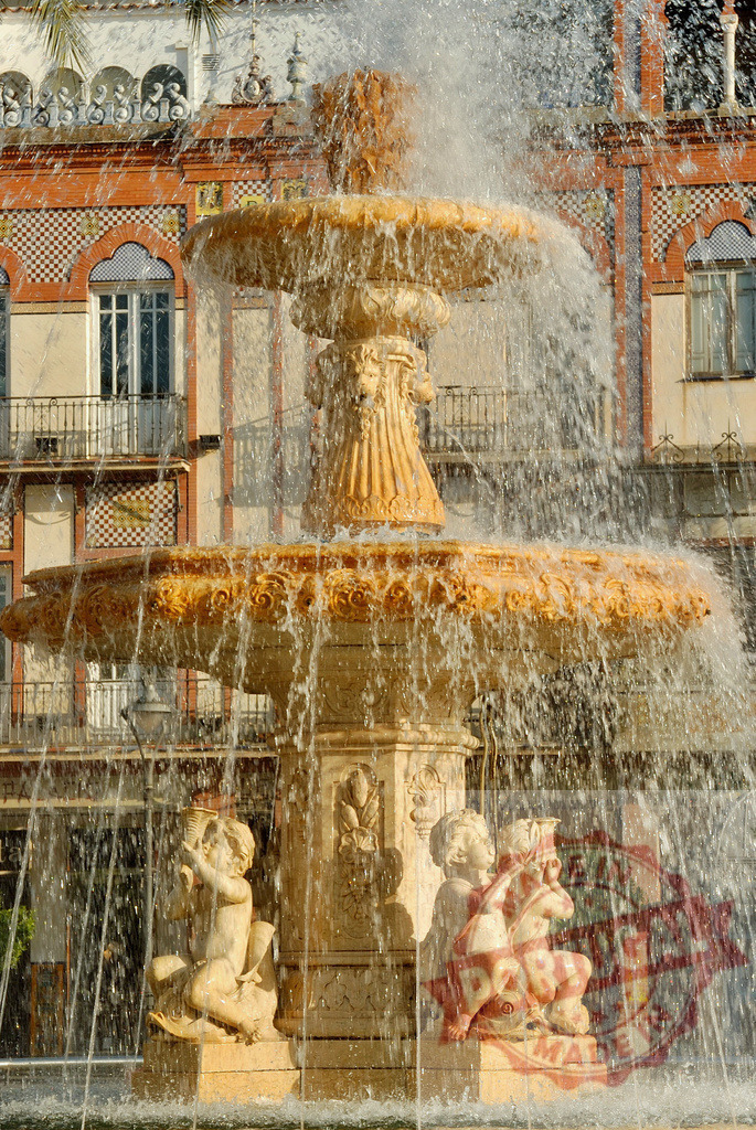 Plaza Alta fountain with cherub sculptures and water splashing. Extremdura - Spain | Historic fountain with playful cherub sculptures splashing water near traditional architecture - Realized with Pictrs.com