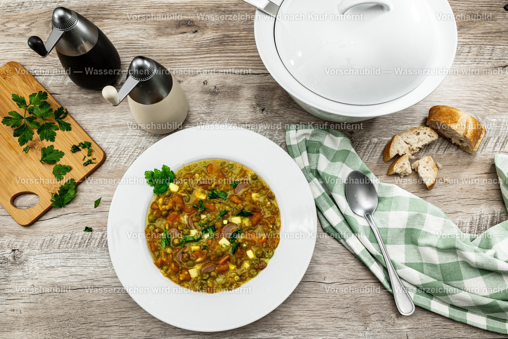Ein Teller deftige Erbsensuppe | Ein Teller deftige Erbsensuppe, dekoriert mit Brot, Tuch, Besteck sowei Salz und Pfeffermühle - Realisiert mit Pictrs.com