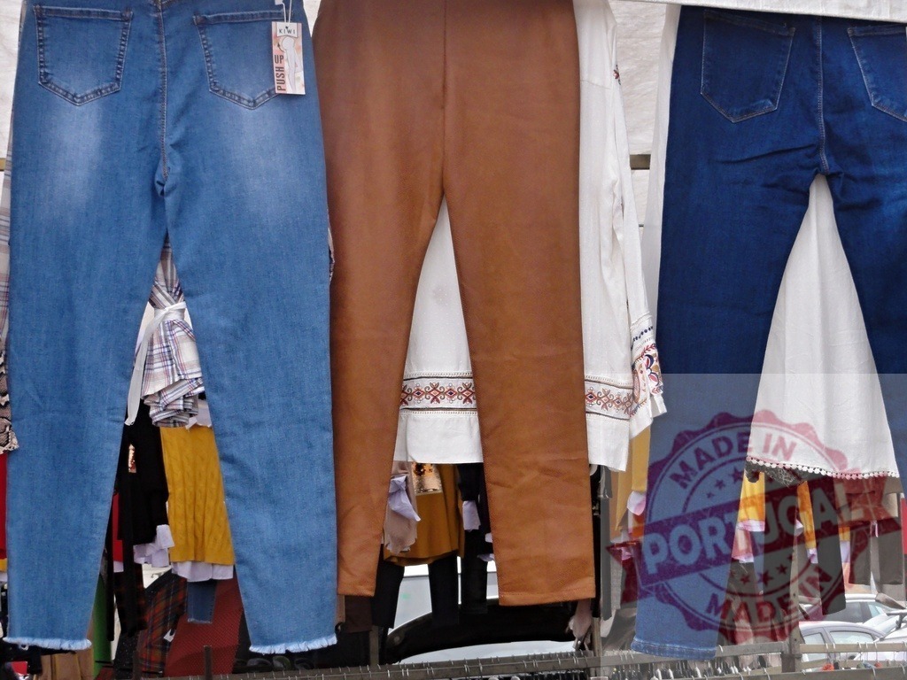 Clothing display with jeans and trousers at outdoor market | Various pants and shirts hanging on a clothes rack at an outdoor market stall - Realized with Pictrs.com