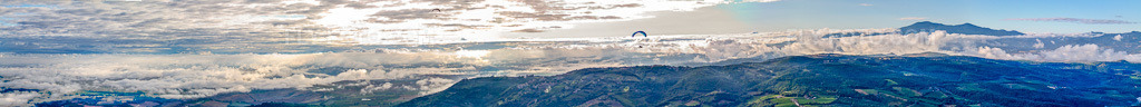 Aerial view: Panorama - Perspective of the peaks in the rocky and mountainous landscape with clouds and paraglider in Montepulciano in the state Siena, Italy. – Photo: IMG_43692-Bearbeitet.jpg taken on 07/28/2011 by Werner Riehm/FLY-FOTO.com – Resolution of the original: 24199 x 2269 px