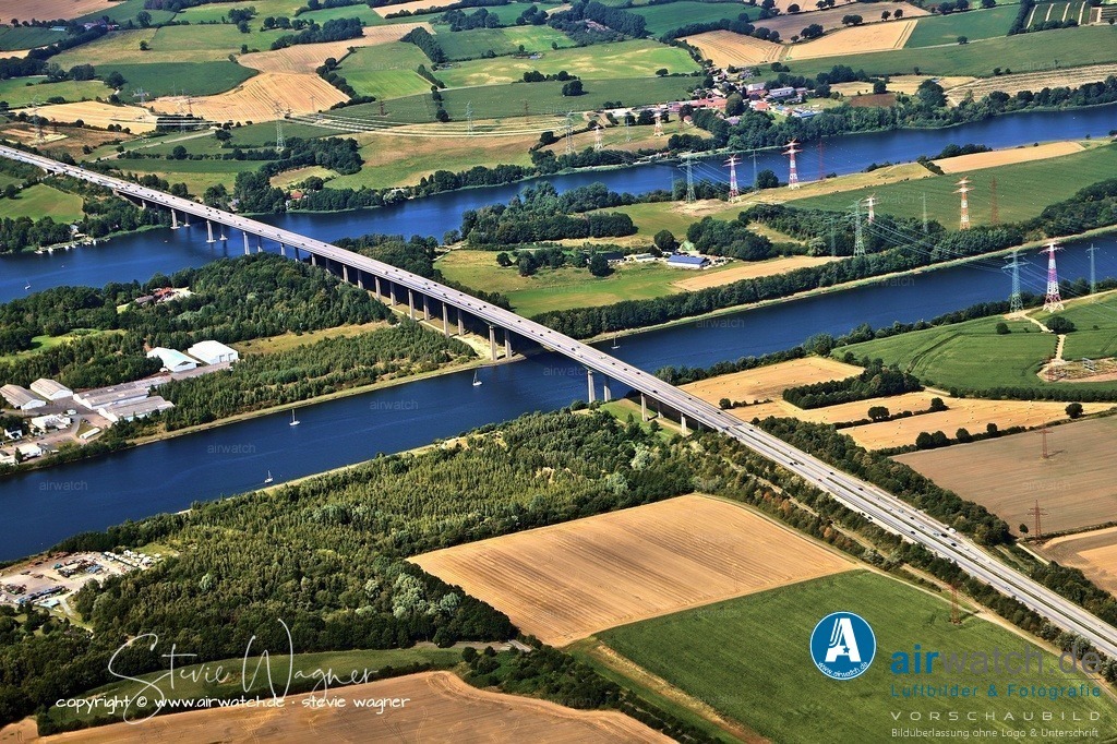 Luftbild Rendsburg - Rader Hochbrücke (A 7) | Die Rader Hochbrücke ist eine 1.498 Meter lange Autobahnbrücke über den Nord-Ostsee-Kanal bei Rendsburg in Schleswig-Holstein. Sie führt die Bundesautobahn 7 (A 7) – Deutschlands längste Autobahn – über den Kanal, die Rader Insel und die Borgstedter Enge. Errichtet von 1969 bis 1972, ist sie nach der Ruhrtalbrücke Mülheim die zweitlängste Straßenbrücke aus Stahl in Deutschland. Aufgrund von Betonschäden und statischen Bedenken wurde ihre Restnutzungsdauer auf 2026 begrenzt.