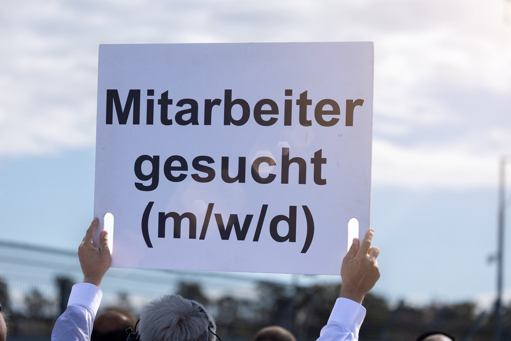 MITARBEITER GESUCHT (M/W/D) Schild | (Fotomontage) Ein Schild mit dem Text MITARBEITER GESUCHT (M/W/D) wird in die Höhe gehalten - Realisiert mit Pictrs.com