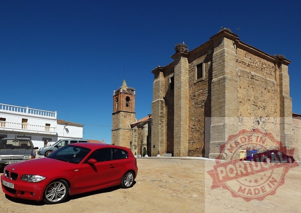 Red BMW car parking at traditional Spanish village square. Spain - Extremadura | Red BMW parked in a village square with an old stone church under a clear blue sky - Realized with Pictrs.com