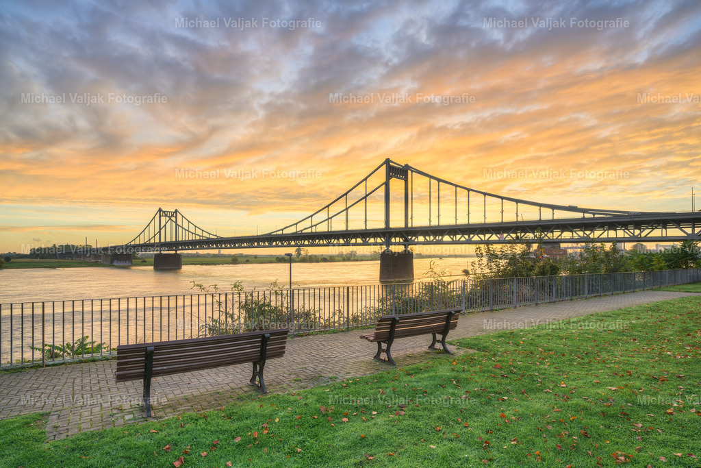 Krefeld-Uerdinger Brücke bei Sonnenaufgang | Die Uerdinger Rheinbrücke, eine Schrägseilbrücke, die den Rhein bei Krefeld-Uerdingen überquert, bietet bei Sonnenaufgang ein besonders malerisches Bild. Die aufgehende Sonne taucht die Umgebung in ein warmes Licht und lässt das Wasser des Flusses glitzern. Die Brücke ist ein wichtiges Verkehrsbauwerk und verbindet die Städte Krefeld und Duisburg, wobei sie täglich von Tausenden genutzt wird. - Realisiert mit Pictrs.com