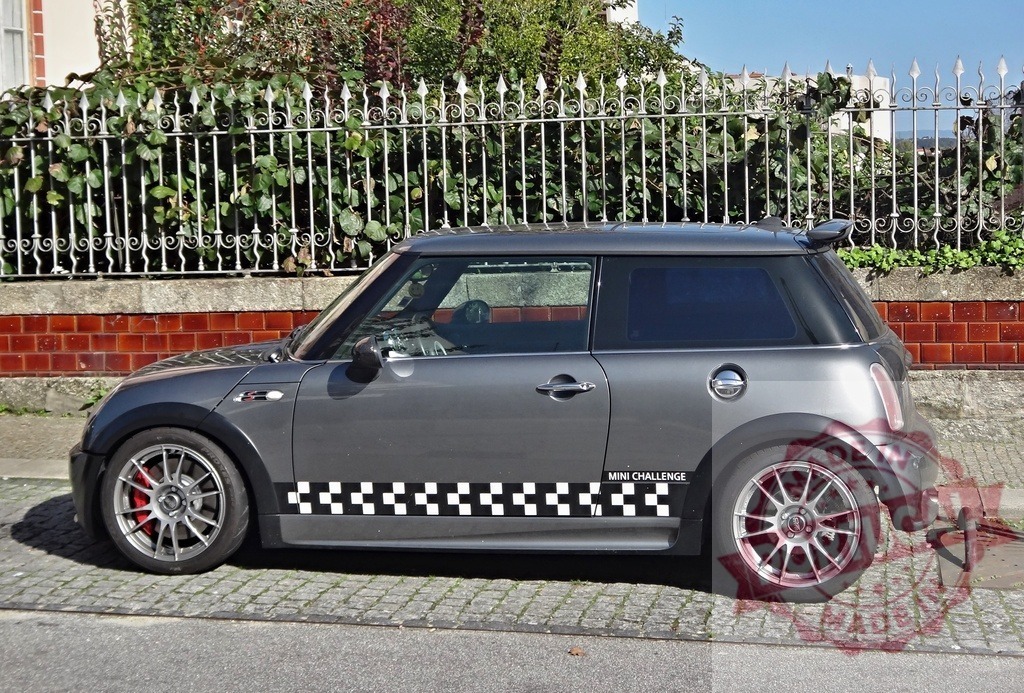 Mini Cooper Challenge car parked by fence | Dark gray Mini Cooper Challenge car parked on a cobblestone street by a decorative fence - Realisiert mit Pictrs.com