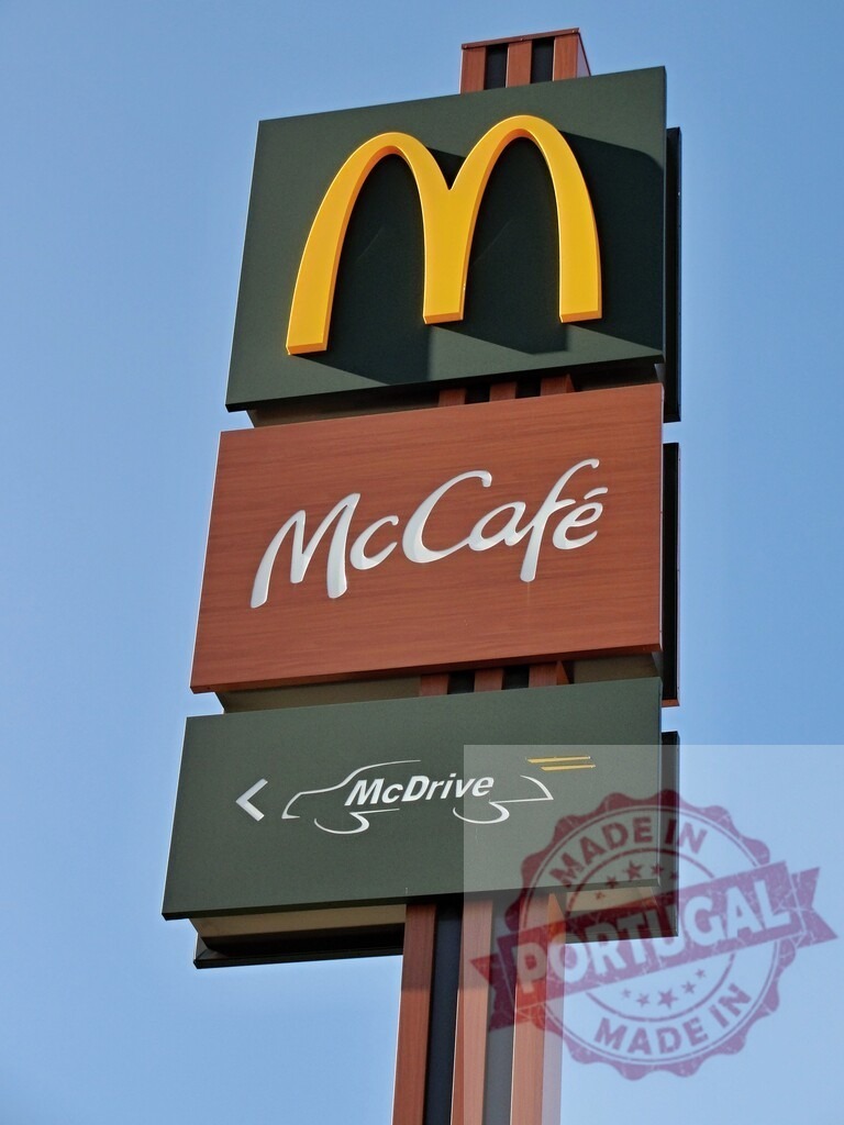 McDonald's sign with golden arches, McCafe and McDrive against blue sky | McDonald's restaurant sign featuring the golden arches, McCafe, and McDrive logos against a clear blue sky - Realisiert mit Pictrs.com
