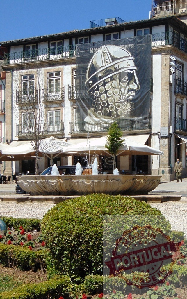 Guimarães city square fountain with Afonso Henriques banner. Region Norte - Portugal | Historic Guimarães square showing fountain and large outdoor banner depicting Afonso Henriques - Realisiert mit Pictrs.com