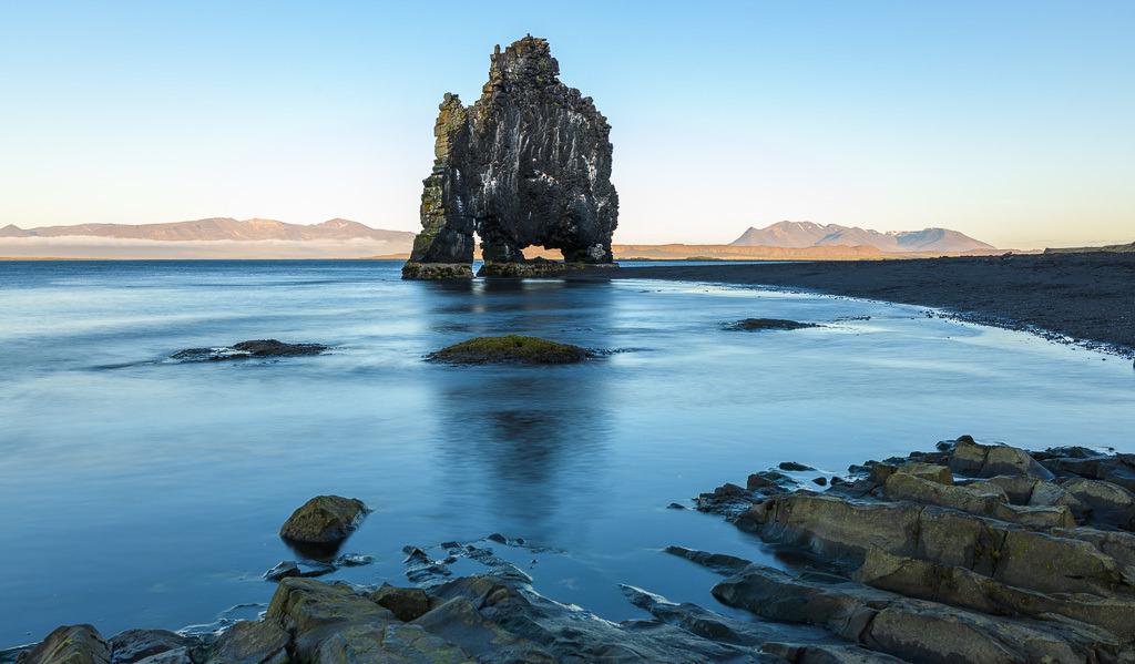 island-2019-163 | Der Hvítserkur (deutsch „weißer Kittel“, da durch Vogelexkremente weiß gefärbt) ist ein Basaltfelsen an der Ostküste der Halbinsel Vatnsnes im Nordwesten von Island. Der etwa 15 Meter hohe Felsen, der an zwei Stellen ausgehöhlt ist, liegt am Húnafjörður und ist Nistplatz verschiedener Vogelarten wie etwa der Dreizehenmöwe und des Eissturmvogels. - Realisiert mit Pictrs.com