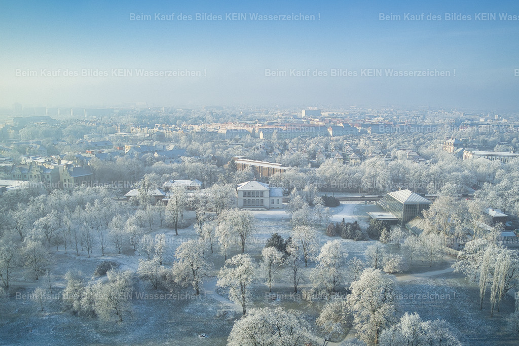 Magdeburg_Luftbild_Winter_Lennepark_Buckau_Klosterbergegarten_Reif_0012_2 | Dieses Luftbild zeigt den Klosterbergegarten in Magdeburg an einem ruhigen Wintermorgen. Eine leichte Schneedecke bedeckt die Wege und Rasenflächen, während die Bäume von einer feinen Schicht Raureif überzogen sind. Die winterliche Landschaft wirkt wie in Weiß gehüllt und verleiht der historischen Parkanlage eine besonders stimmungsvolle Atmosphäre.Im Mittelpunkt der Aufnahme liegt das Gesellschaftshaus, das sich sanft aus dem leichten Morgennebel erhebt. Die ersten Sonnenstrahlen des Tages durchbrechen die Nebelschwaden und tauchen die Szene in ein weiches, diffuses Licht. Dadurch entsteht eine fast märchenhafte Stimmung, die den besonderen Charakter dieses Augenblicks eindrucksvoll unterstreicht.Aus der Vogelperspektive werden die harmonischen Strukturen des Klosterbergegartens sichtbar, der als ältester Volksgarten Deutschlands zu den bedeutendsten Parkanlagen Magdeburgs zählt. Die Kombination aus verschneiter Landschaft, vereisten Bäumen, aufziehendem Morgenlicht und dem historischen Gesellschaftshaus macht dieses Luftbild zu einem außergewöhnlichen Blick auf die winterliche Schönheit der Landeshauptstadt Sachsen-Anhalts. - Realisiert mit Pictrs.com