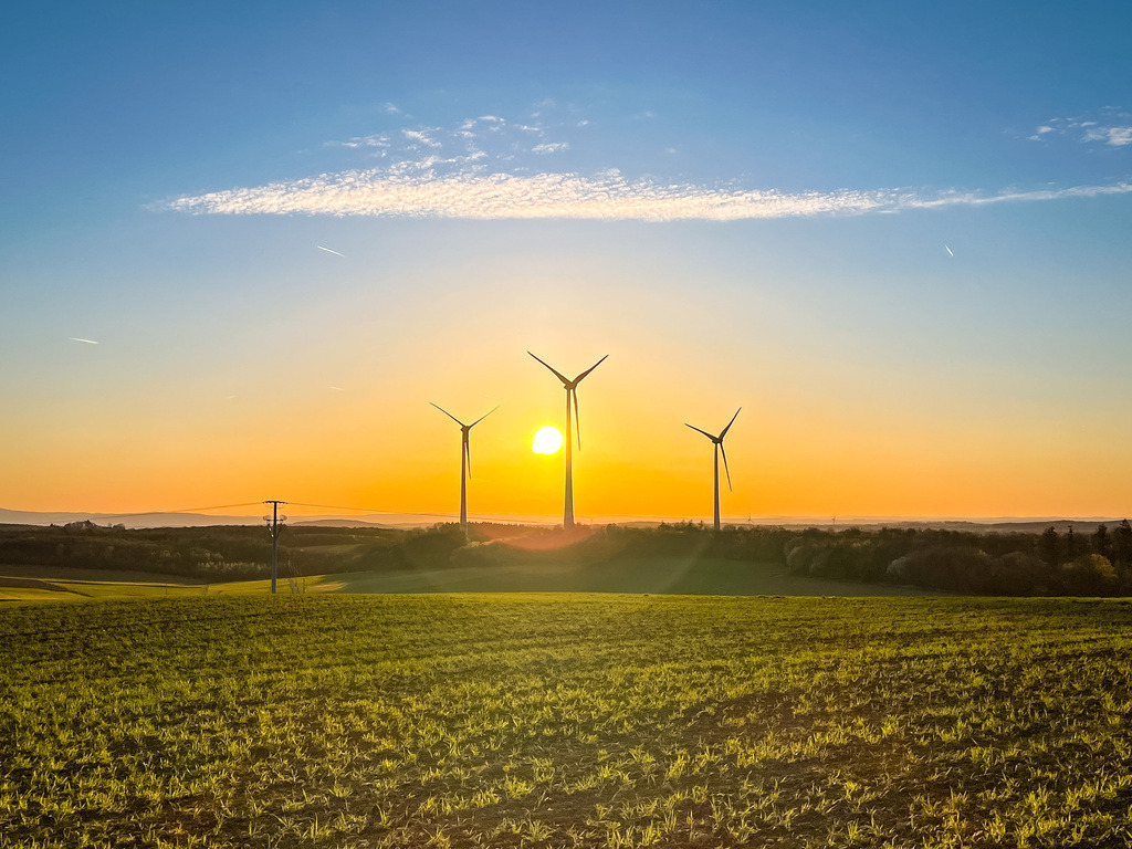 Kontraste am Horizont | Wenn die Sonne hinter den Hügeln versinkt und ihr goldenes Licht die Landschaft in ein warmes Leuchten taucht, können sogar Gegensätze harmonieren. Sonst oftmals verschmähte Windräder fügen sich in dieser Zeit nahtlos in die Landschaft ein und die Welt erscheint im Gleichgewicht. Es entsteht eine Symbiose aus Technik und weist den Weg zu einer nachhaltigen Welt ist. - Realisiert mit Pictrs.com