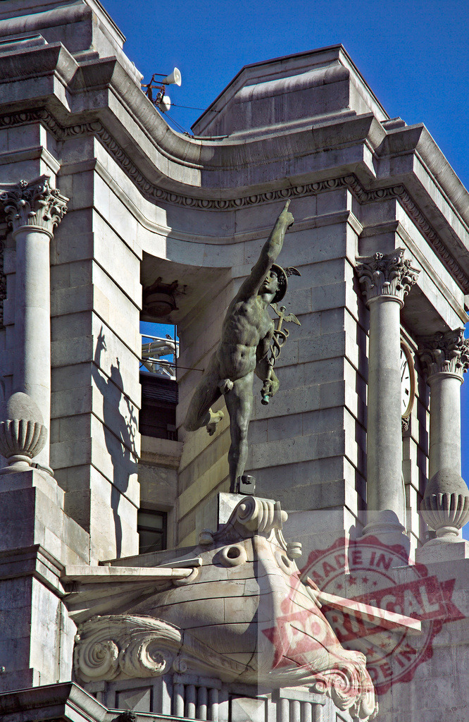 Mercury statue gracing classic building facade against sky. Spain - Bilbao | Bronze statue of Mercury the messenger god adorning a classical building facade - Realized with Pictrs.com