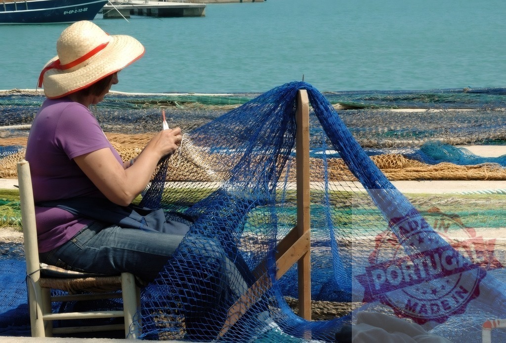Woman mending blue fishing net by harbor | Woman in straw hat sitting by the sea, repairing a traditional fishing net - Realisiert mit Pictrs.com