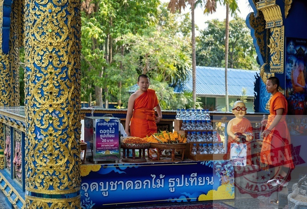 Young Buddhist Monks Selling Offerings at Wat Rong Suea Ten, Chiang Rai, Thailand | Two young monks standing at a stall, selling flowers, candles, and water bottles at the beautifully decorated Wat Rong Suea Ten - Realisiert mit Pictrs.com