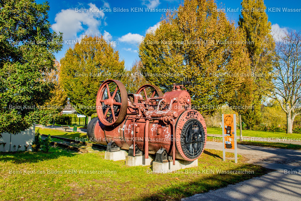 Magdeburg Sehenswürdigkeiten Dampfmaschine in Buckau Sülzehafen Wolf AG-2574 | Das Foto zeigt eine historische Dampfmaschine im Sülzehafen Magdeburg aus einer bodennahen Perspektive. Die massive Gusskonstruktion mit Schwungrad, Pleuelstangen und Ventilsteuerung vermittelt eindrucksvoll die Ingenieurkunst des Industriezeitalters. Durch die niedrige Kameraposition treten die technischen Details und die imposanten Abmessungen der Maschine besonders deutlich hervor.Die Dampfmaschine wurde von der Magdeburger Maschinenbaufabrik Wolf AG gefertigt, einem der bedeutendsten Maschinenbauunternehmen Deutschlands. Die Wolf AG entwickelte seit dem späten 19. Jahrhundert leistungsstarke Dampfmaschinen für Mühlen, Fabriken und Kraftwerke. Solche stationären Maschinen erreichten je nach Ausführung Leistungen von mehreren hundert Pferdestärken und bildeten über Jahrzehnte das Herzstück industrieller Produktionsanlagen. Das große Schwungrad sorgte für einen gleichmäßigen Lauf und speicherte die Bewegungsenergie, während die Kraft über Transmissionen auf die angeschlossenen Maschinen übertragen wurde.Die Aufnahme dokumentiert ein bedeutendes technisches Denkmal der Magdeburger Industriegeschichte. Die historische Dampfmaschine steht stellvertretend für die Innovationskraft des Magdeburger Maschinenbaus und erinnert an eine Zeit, in der dampfbetriebene Antriebe die industrielle Entwicklung maßgeblich vorantrieben. - Realisiert mit Pictrs.com