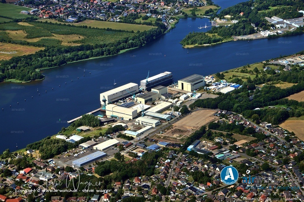 Luftbild Rendsburg - Die Lürssen Werft Bremen GmbH & Co. KG, bis 2025 bekannt als Fr. Lürssen Werft | Die Lürssen Werft Bremen GmbH & Co. KG, bis 2025 bekannt als Fr. Lürssen Werft, ist eine deutsche Schiffswerft mit Hauptsitz im Bremer Stadtteil Vegesack und weiteren Schiffbaueinrichtungen in Lemwerder, Berne, Schacht-Audorf und Fähr-Lobbendorf. Die Werft wurde am 27. Juni 1875 von Friedrich Lürßen gegründet und begann mit der Produktion von Arbeitsbooten für die Fischerei und Fährbetrieb. Seit den 1880er Jahren erweiterte sich das Sortiment auf Sportboote, wobei 1886 das erste Motorboot der Welt, die Rems, gebaut wurde. er Schwerpunkt verschob sich im 20. Jahrhundert zunehmend hin zum Motorbootsbau, wobei Lürssen zu einer führenden deutschen Motorbootwerft avancierte.