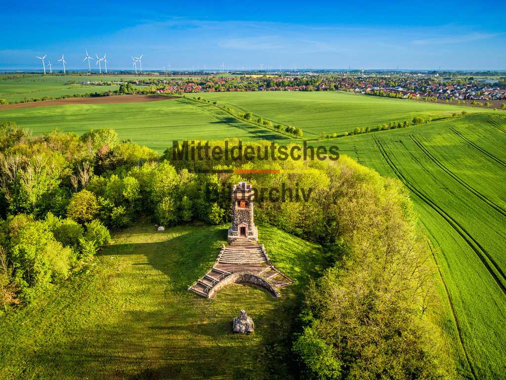 Wartberg Niederndodeleben mit Bismarckwarthe-0025 | Dieses Luftbild zeigt die Bismarckwarte auf dem Wartberg bei Niederndodeleben westlich von Magdeburg in Sachsen-Anhalt aus einer eindrucksvollen Drohnenperspektive. Der historische Aussichtsturm erhebt sich auf einer der markantesten Erhebungen der Magdeburger Börde und bietet einen weiten Blick über die umliegende Landschaft. Aus der Luft wird die besondere Lage des Bauwerks inmitten der offenen Kulturlandschaft besonders deutlich sichtbar.Die Bismarckwarte gehört zu den zahlreichen Aussichtstürmen, die zu Ehren des ehemaligen Reichskanzlers Otto von Bismarck errichtet wurden. Der markante Turm ist bis heute ein bekanntes Wahrzeichen der Region und ein beliebtes Ausflugsziel. Seine erhöhte Lage macht ihn weithin sichtbar und verleiht dem Wartberg eine besondere Bedeutung innerhalb der ansonsten sanft gewellten Bördelandschaft.Besonders beeindruckend wirkt die Weite der Umgebung. Rund um den Wartberg erstrecken sich die fruchtbaren Felder der Magdeburger Börde bis zum Horizont. Die geometrischen Strukturen der Ackerflächen, die Feldwege und die wenigen Baumgruppen verleihen der Aufnahme eine außergewöhnliche Ruhe und Großzügigkeit. Aus der Vogelperspektive wird die einzigartige Weite dieser Landschaft eindrucksvoll erlebbar.Dieses Luftbild zeigt die Bismarckwarte als markanten Orientierungspunkt in einer der fruchtbarsten Kulturlandschaften Deutschlands und vermittelt einen faszinierenden Eindruck von Sachsen-Anhalts weiter Bördelandschaft. - Realisiert mit Pictrs.com