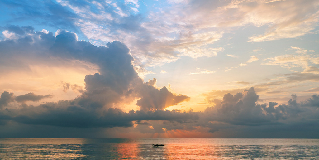 Cineastischer Sonnenuntergang am Meer (Panorama) | Kenia | Premium-Wandbild im Panorama-Format von justsomewhere.com: Ein spektakulärer Pastell-Sonnenuntergang in Kenia mit dramatischen Wolken, durchbrechenden Lichtstrahlen und einem kleinen Fischerboot auf dem ruhigen Indischen Ozean. - Realisiert mit Pictrs.com
