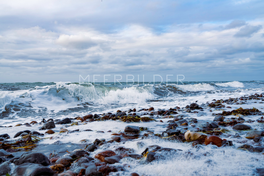 Ostseebild Steilküste Wustrow | Die malerische Ostsee zeigt sich lebhaft und temperamentvoll, direkt unterhalb der Steilküste von Wustrow. In diesem Ostseebild sind die aufbrausenden Wellen zu sehen, wie sie energisch an den Kiesstrand branden. Man kann förmlich das Grollen des abfließenden Wassers über die Steine hören. Hier und da findet man Seegras am Strand angespült und eine zarte Schaumkrone bedeckt die Steine. Um einen besonderen Effekt zu erzielen, wurde bewusst im unteren und rechten Bereich des Bildes mit einer leichten Unschärfe gearbeitet. Dieses schöne Ostseebild empfehlen wir entweder als Alu-Dibond-Druck oder als Leinwandbild.