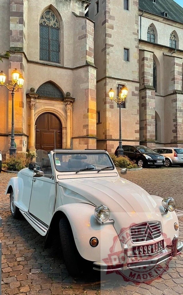 White Citroën 2CV parked near Temple Saint-Étienne in Mulhouse, France | Classic white Citroën 2CV parked on cobblestone street near illuminated Temple Saint-Étienne in Mulhouse, France - Realisiert mit Pictrs.com