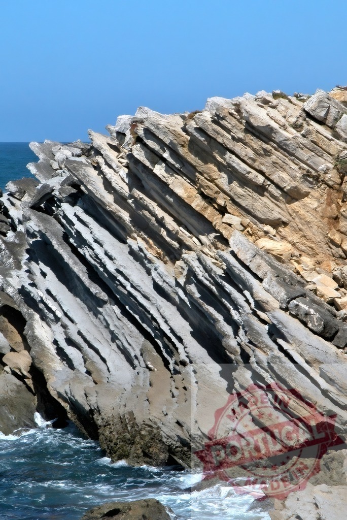 Baleal geological rock formation showing tilted sedimentary strata. Centro Portugal | Sedimentary rock layers forming a coastal cliff with visible tilted strata and ocean waves - Realisiert mit Pictrs.com