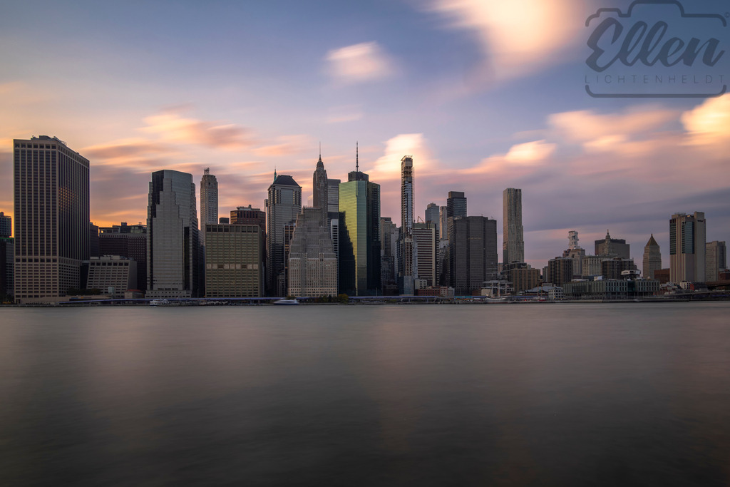 Whispers of Light | Soft clouds sweep across the sky as evening light caresses Manhattan’s skyline. The calm water mirrors the city’s glow, capturing a moment of stillness in the rhythm of New York. - Realisiert mit Pictrs.com