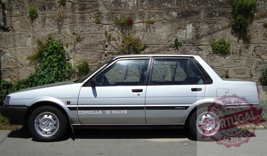 Silver Toyota Corolla 12 Valve parked near stone wall | Classic silver Toyota Corolla 12 Valve parked on the side of the road next to a stone wall with some vegetation growing on it - Realisiert mit Pictrs.com