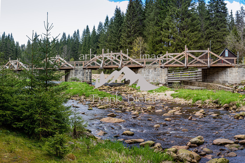OE7A5472-Pano | Die 72 m lange Brücke wurde zwischen 1799 und 1800 unter der Leitung des Fürstlich-Schwarzenbergischen Forstingenieurs Joseph Rosenauer als Eingangsbauwerk des Chinitz-Tettauer Schwemmkanals errichtet. Mittels von der Brücke in den Fluss hineingerammter Rundholzrechen wurde das vom Böhmerwaldkamm heruntergeflößte Stammholz abgefangen und aus der wegen der zahlreichen mächtigen Felsblöcke für die Flößerei untauglichen Vydra in den Schwemmkanal abgeleitet.