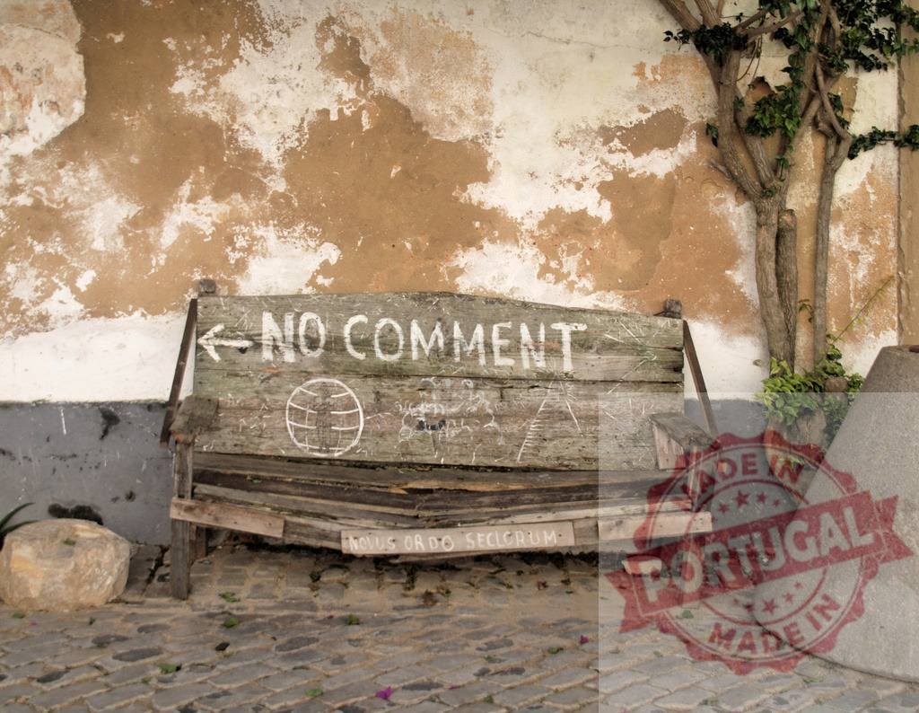 Old wooden bench displaying no comment street art | Aged wooden bench with graffiti NO COMMENT against weathered plaster wall - Realized with Pictrs.com